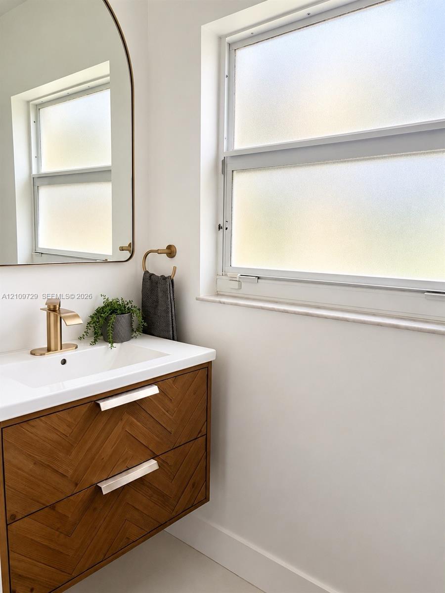 Wall-mounted vanity featuring a chevron-patterned wood-finish exterior, integrated white sink, metallic-finish faucet, and arched mirror