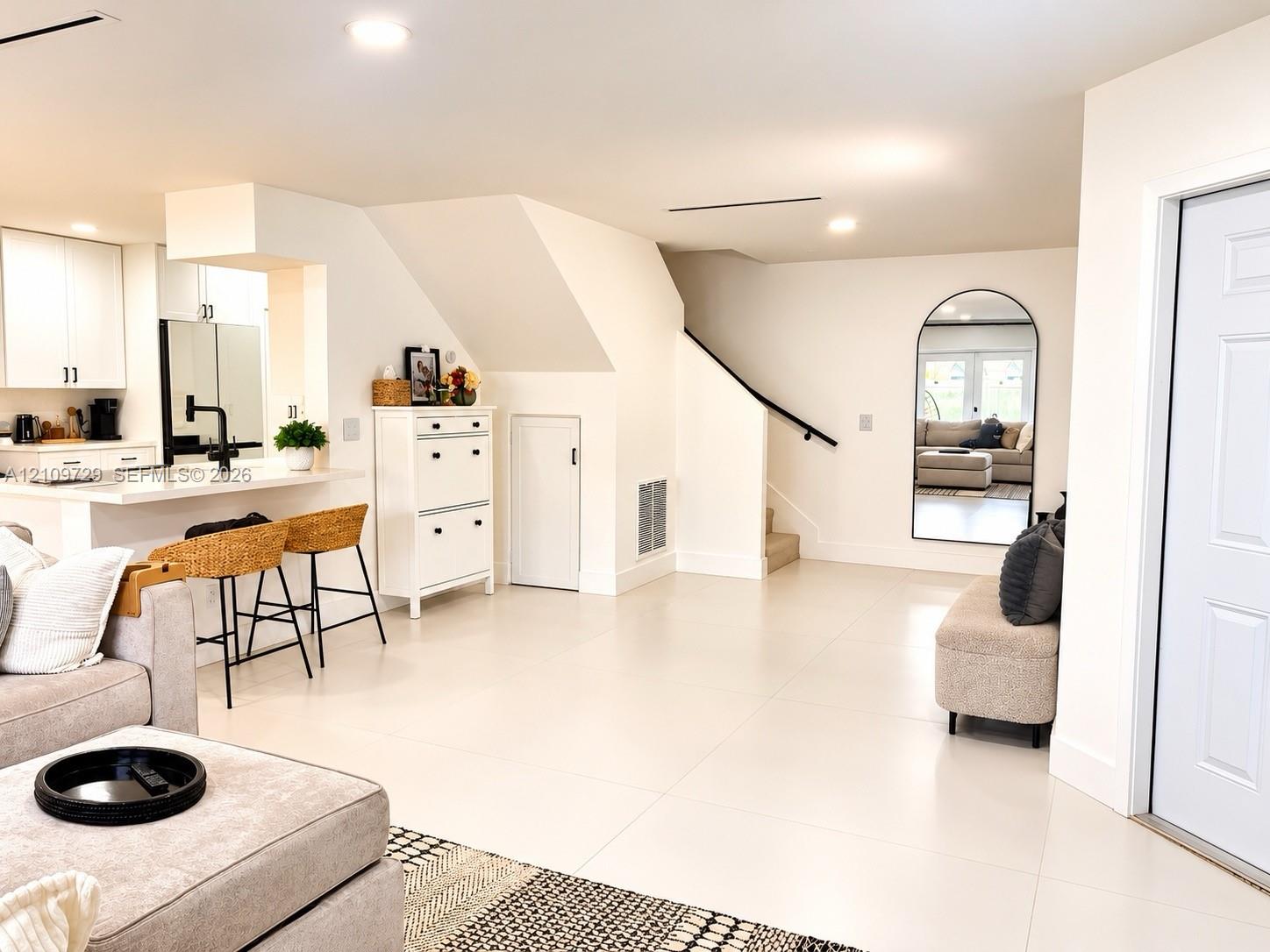 Open-concept interior featuring large-format tile flooring, recessed lighting, breakfast bar with quartz countertop, and arched wall mirror