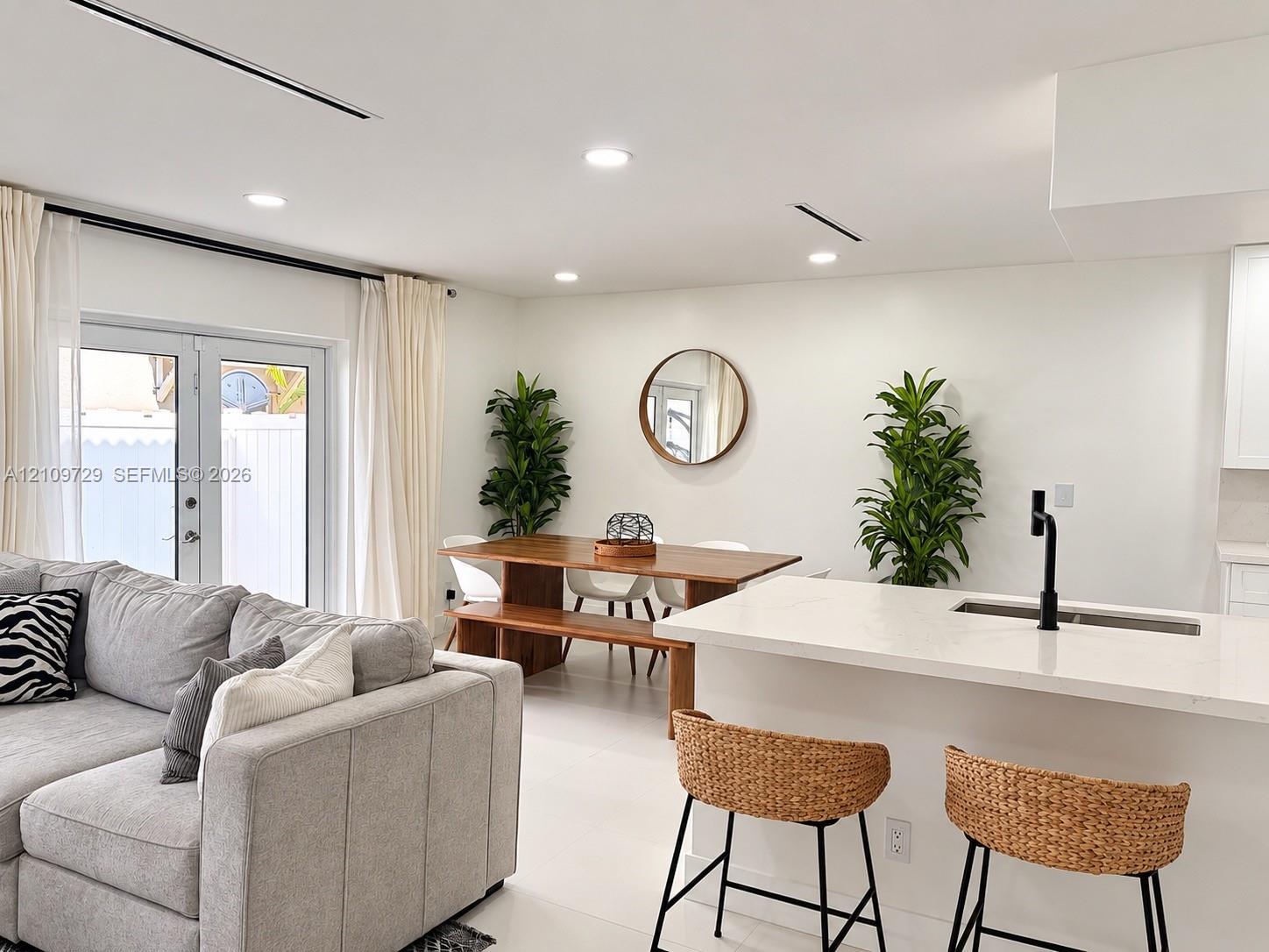 Open-concept living space featuring a central kitchen island with a light-toned countertop, matte black faucet, recessed ceiling lighting, and glass-paneled double doors