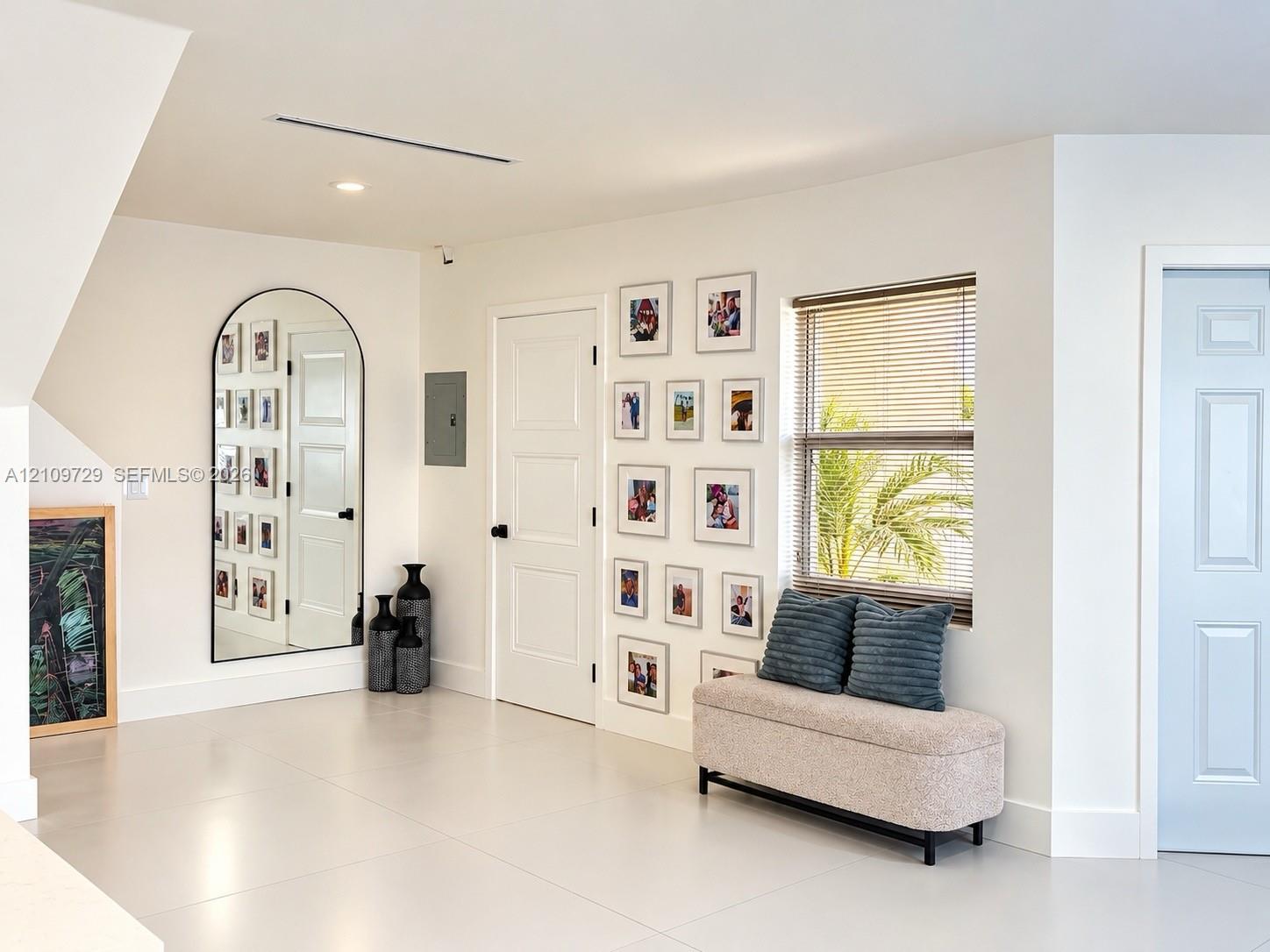 Neutral-toned tile flooring, arched wall mirror with a slender black frame, recessed ceiling lighting, and solid-core interior doors with matte black hardware
