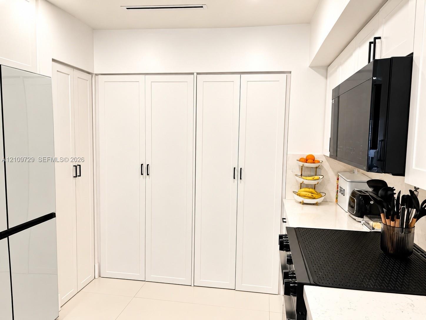 Custom white cabinetry with matte black hardware, stone-finish countertops, and integrated black appliances