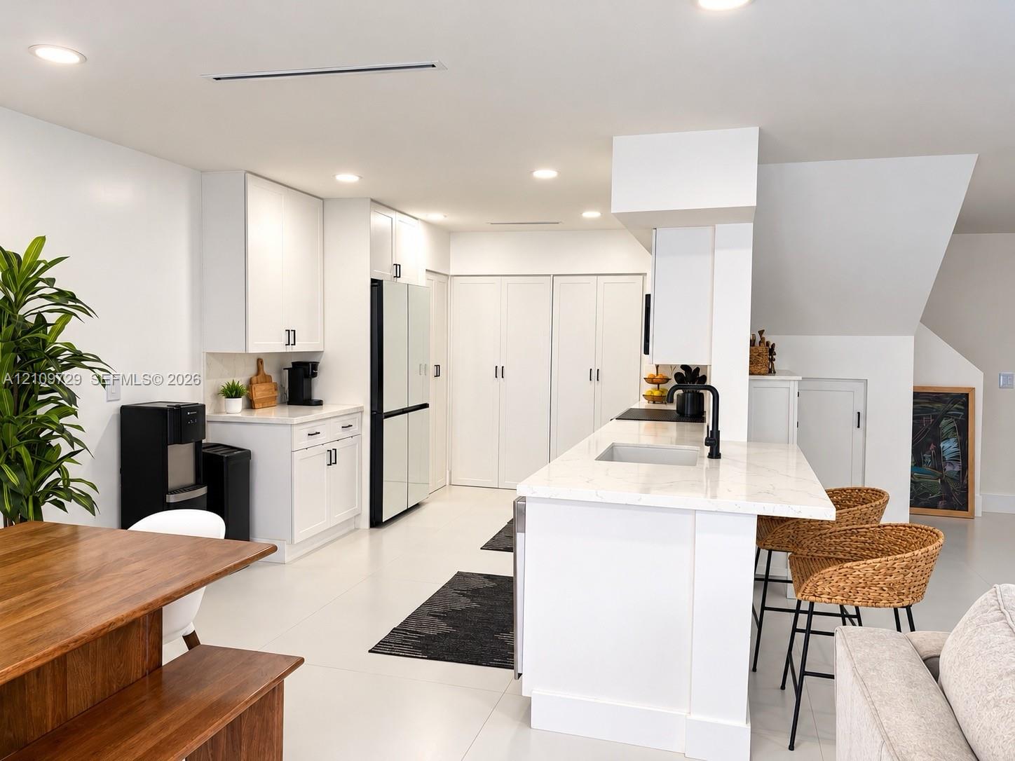 Kitchen featuring white shaker-style cabinetry, quartz countertops, a central island with a built-in sink, matte black hardware, and recessed ceiling lighting