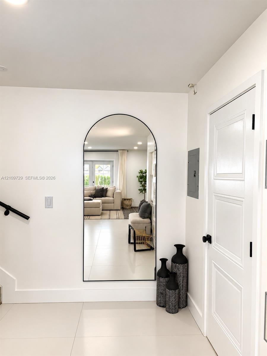 Large arched wall mirror with a matte black frame, light-toned tile flooring, and a multi-panel door with matte black hardware