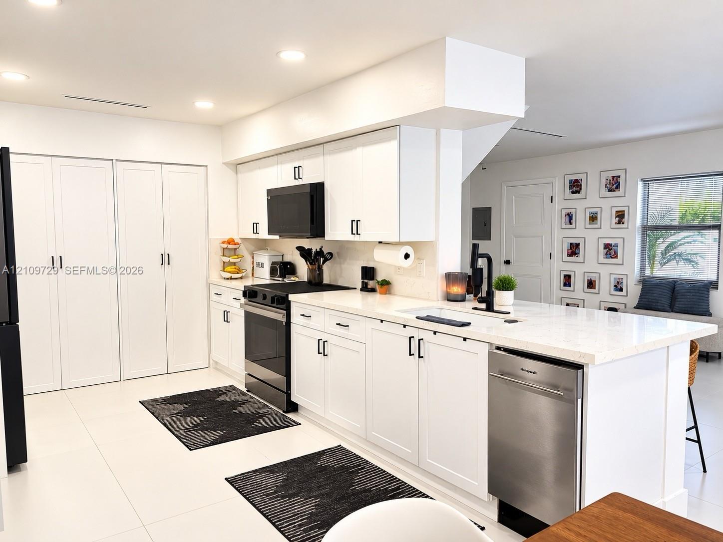 Kitchen featuring white cabinetry with matte black hardware, stone-surface countertops, a center island with a built-in dishwasher, and a suite of black appliances