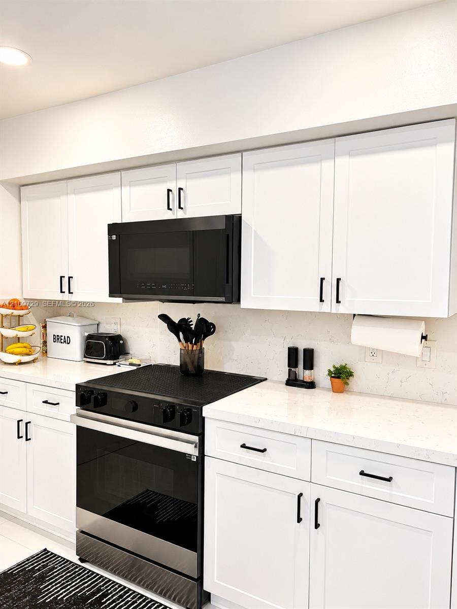 Kitchen featuring white shaker-style cabinetry, solid-surface countertops, a neutral stone-patterned backsplash, and matte black hardware