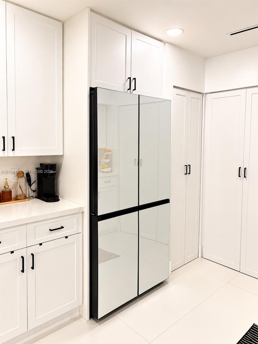 Custom white cabinetry with matte black hardware, floor-to-ceiling pantry storage, and a four-door refrigerator with mirrored finish panels