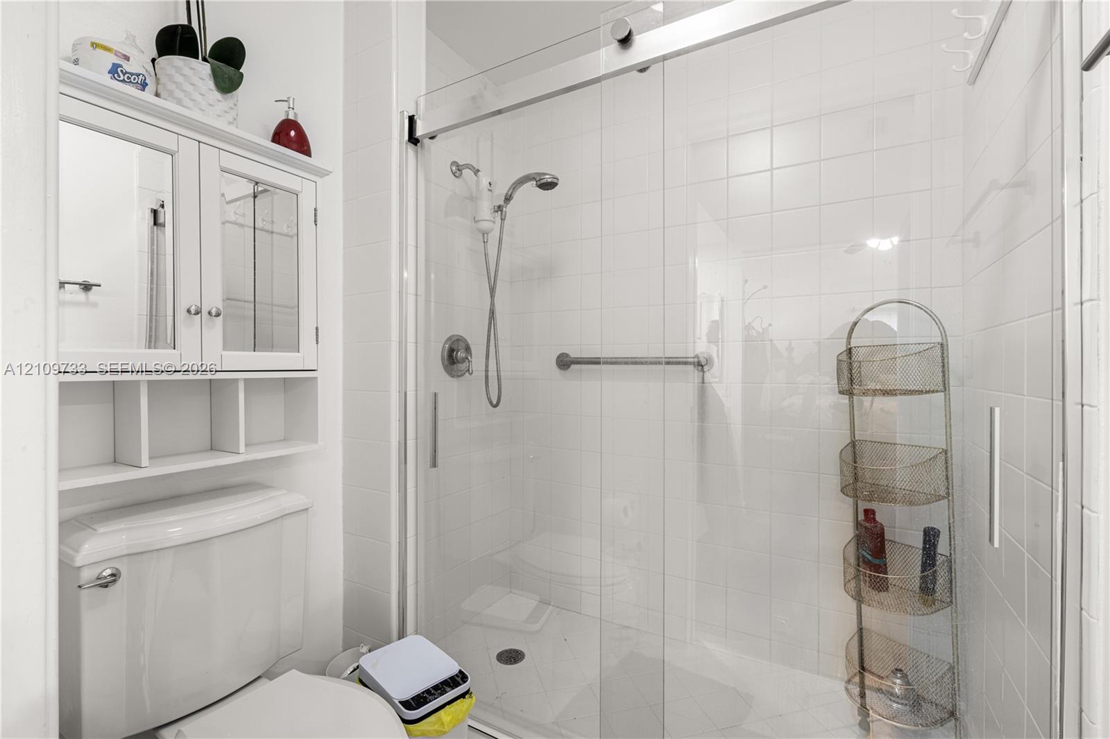 Walk-in shower with sliding glass door, white wall tiling, chrome shower fixtures, and built-in medicine cabinet with integrated shelving