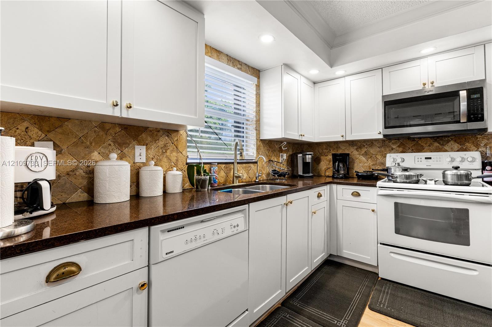 Kitchen featuring white cabinetry, stone-finish countertops, diagonal-set stone backsplash, recessed lighting, and stainless steel microwave Kitchen featuring white cabinetry, stone-finish countertops, diagonal-set stone backsplash, recessed lighting, and stainless steel microwave