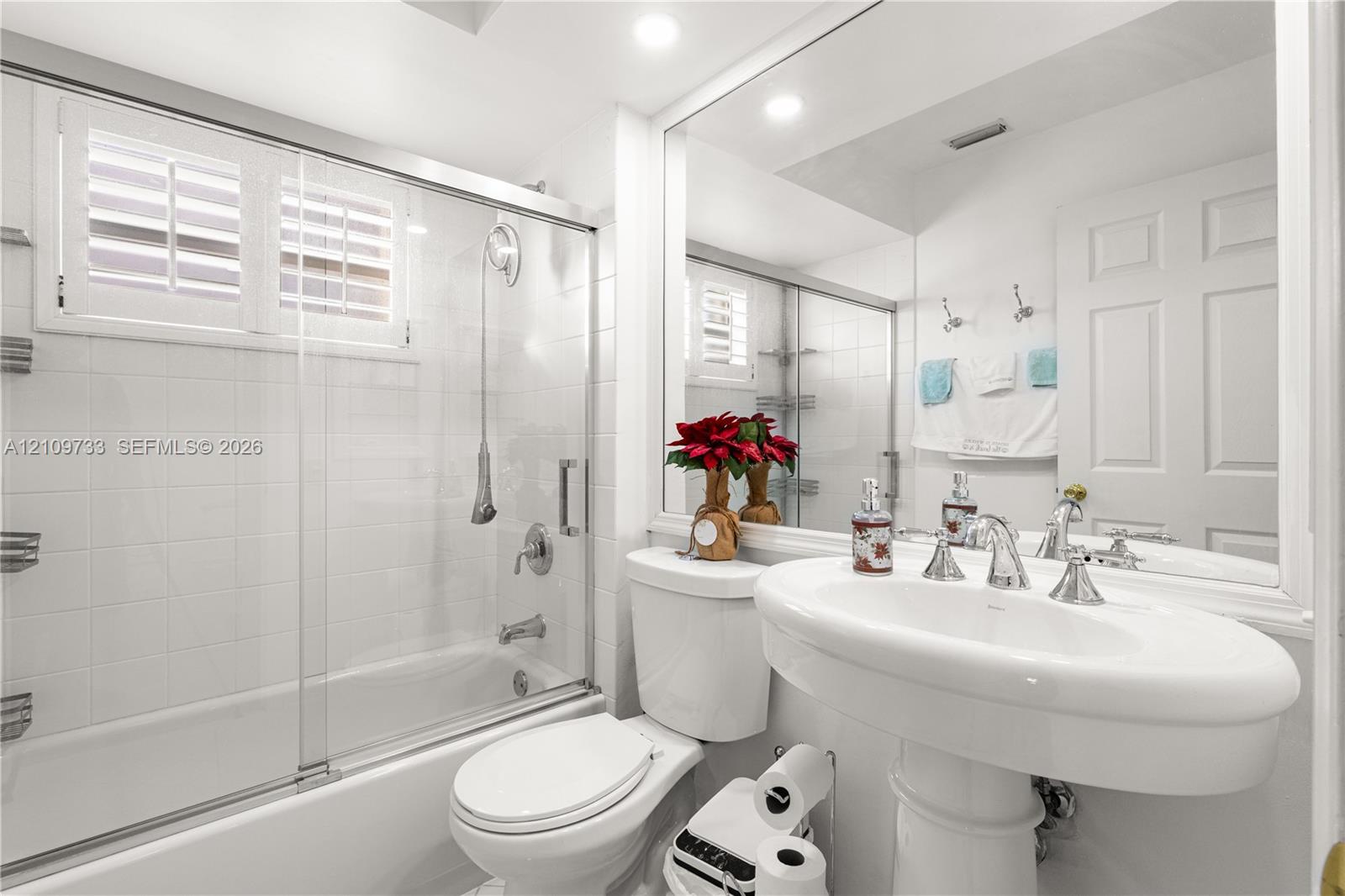 Bathroom featuring a shower-tub combination with a sliding glass door, white wall tiling, a pedestal sink with polished chrome fixtures, and a large-format mirror