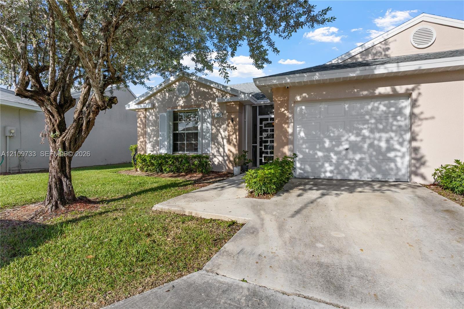 Stucco exterior featuring a concrete driveway, attached single-car garage, manicured lawn, and mature landscaping