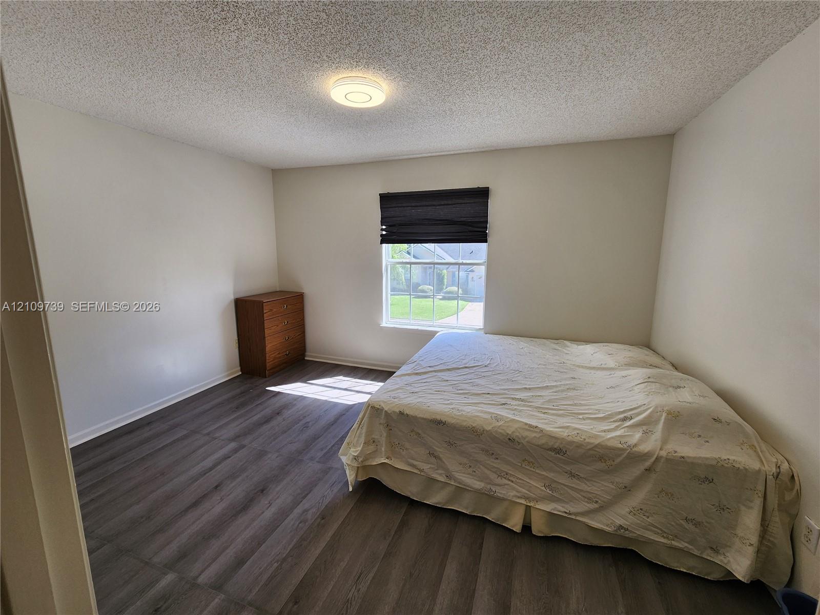 Room featuring wood-finish flooring, a single window, and a central flush-mount ceiling light fixture
