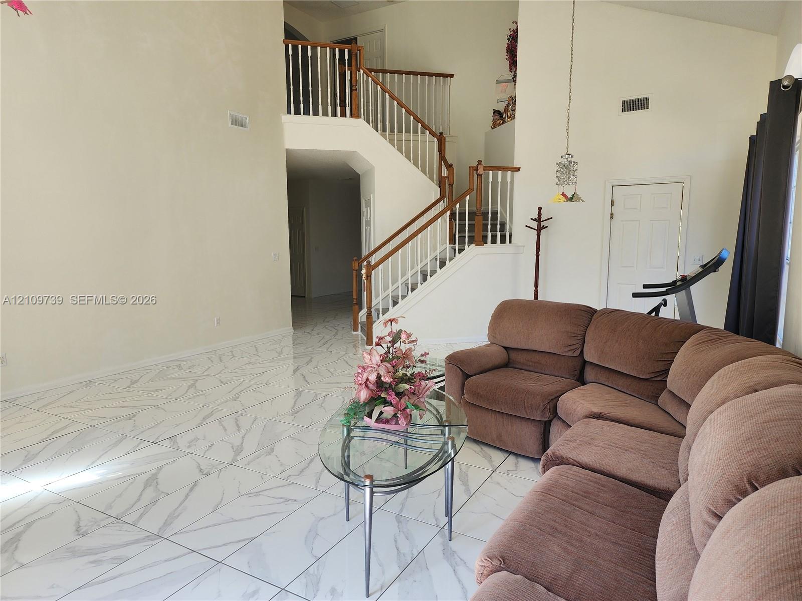 High-ceiling interior featuring large-format tile flooring with a veined pattern and a central staircase with wooden handrails and balusters High-ceiling interior featuring large-format tile flooring with a veined pattern and a central staircase with wooden handrails and balusters