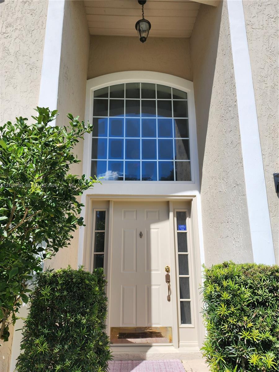 Stucco entryway featuring a paneled door, sidelights, an arched transom window, and a hanging pendant fixture Stucco entryway featuring a paneled door, sidelights, an arched transom window, and a hanging pendant fixture
