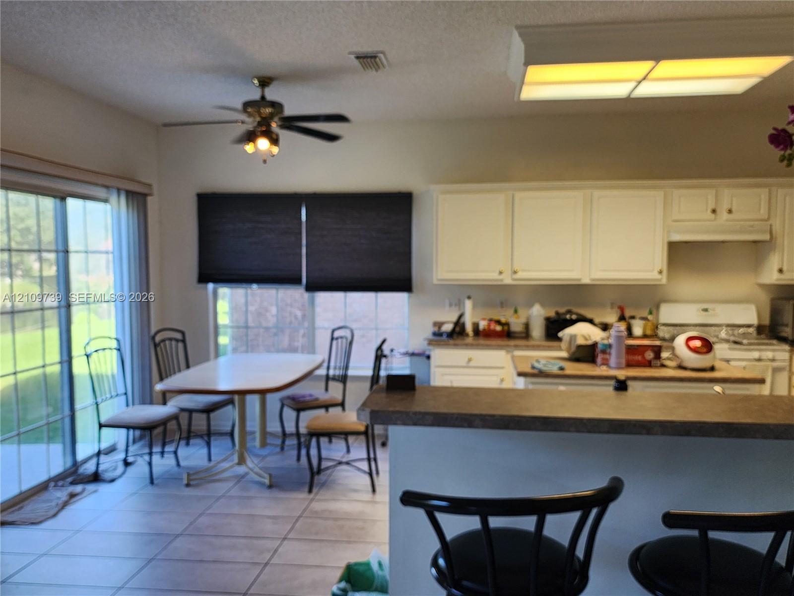 Kitchen featuring white cabinetry, a breakfast bar with a solid surface countertop, tile flooring, a ceiling fan with integrated lighting, and sliding glass doors