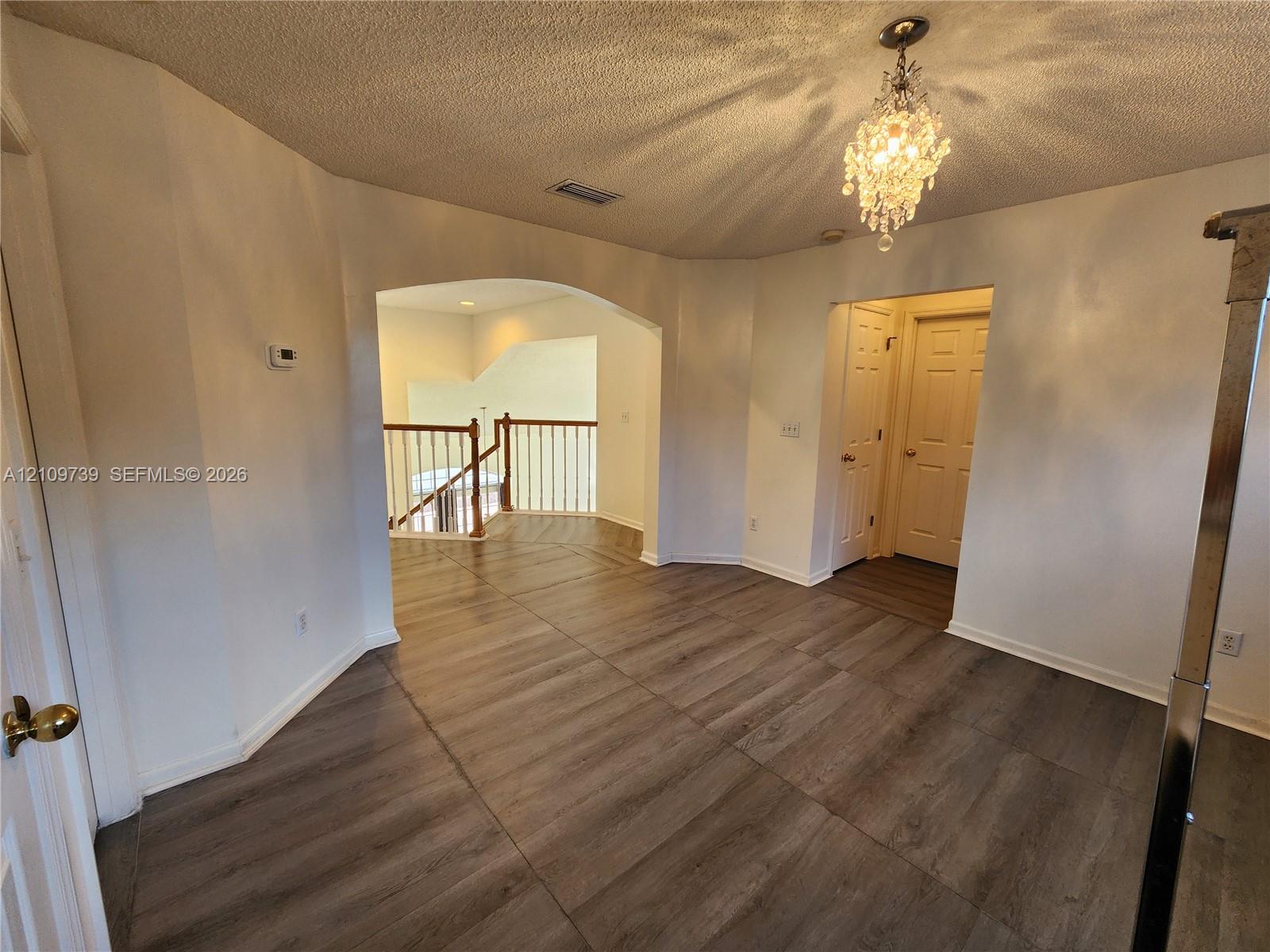 Wood-finish flooring, ornate crystal chandelier, arched entryway, and wooden staircase railing