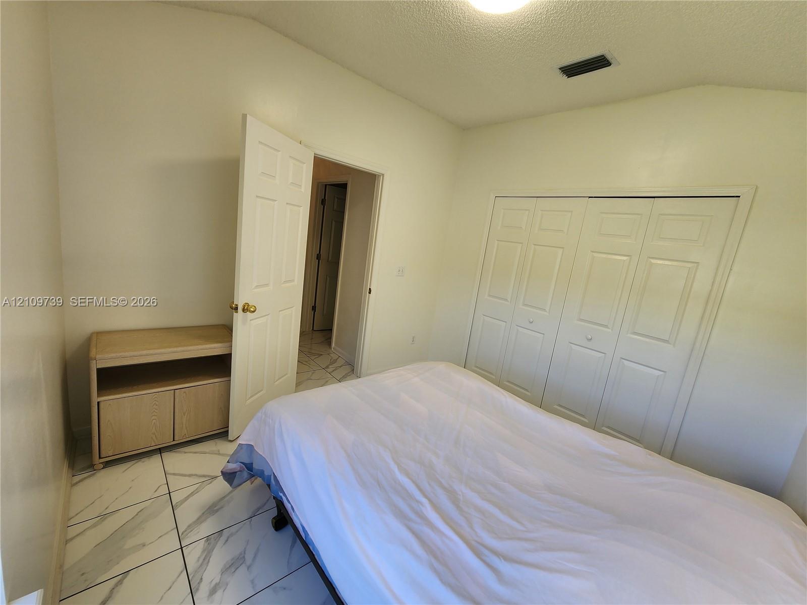 Room featuring large-format tile flooring with marble-patterned finish, multi-panel closet doors, and solid-core interior doors with brass-tone hardware