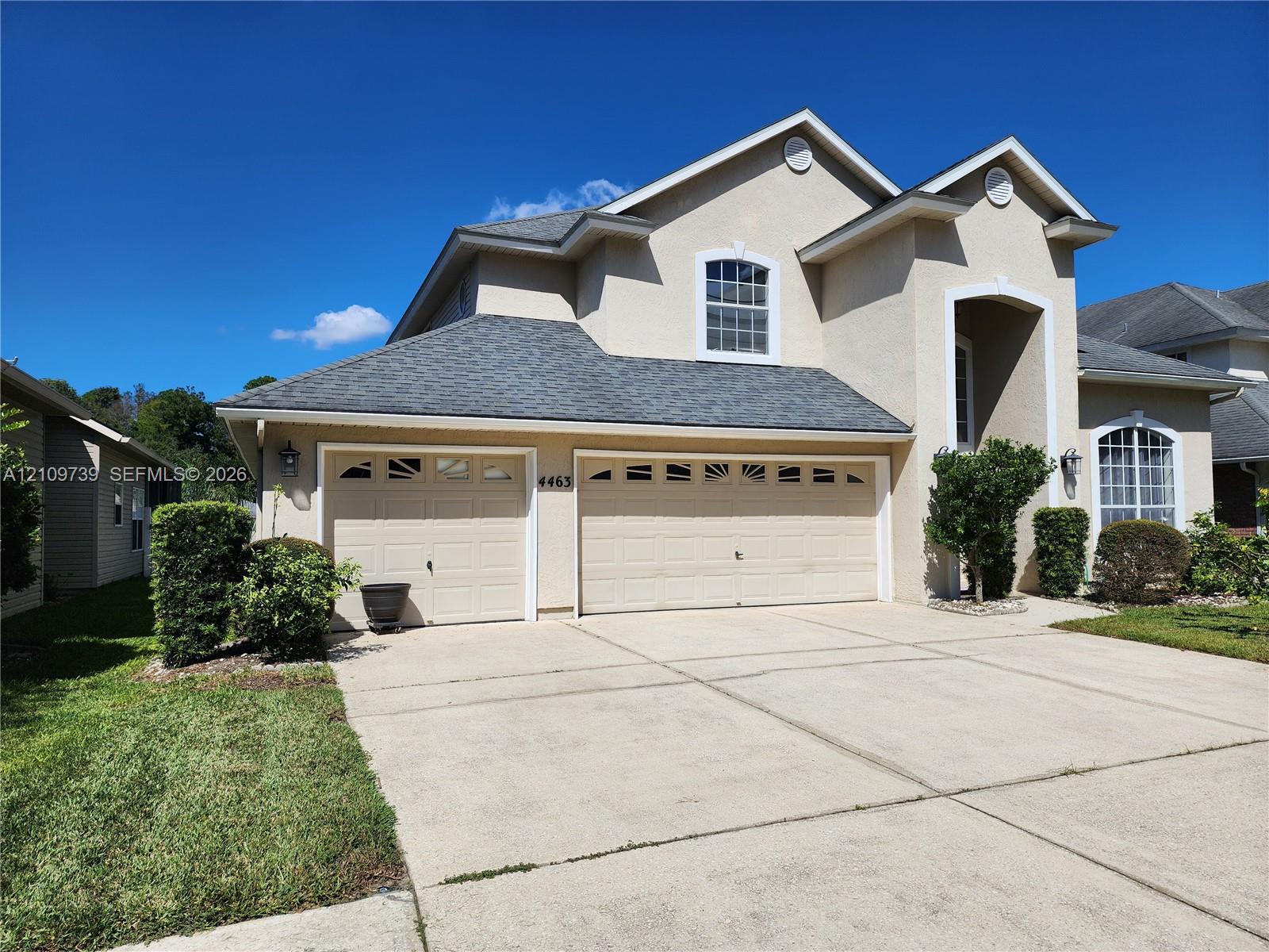Two-story stucco exterior featuring a gabled roofline, arched window detailing, and a three-car garage with decorative transom windows Two-story stucco exterior featuring a gabled roofline, arched window detailing, and a three-car garage with decorative transom windows