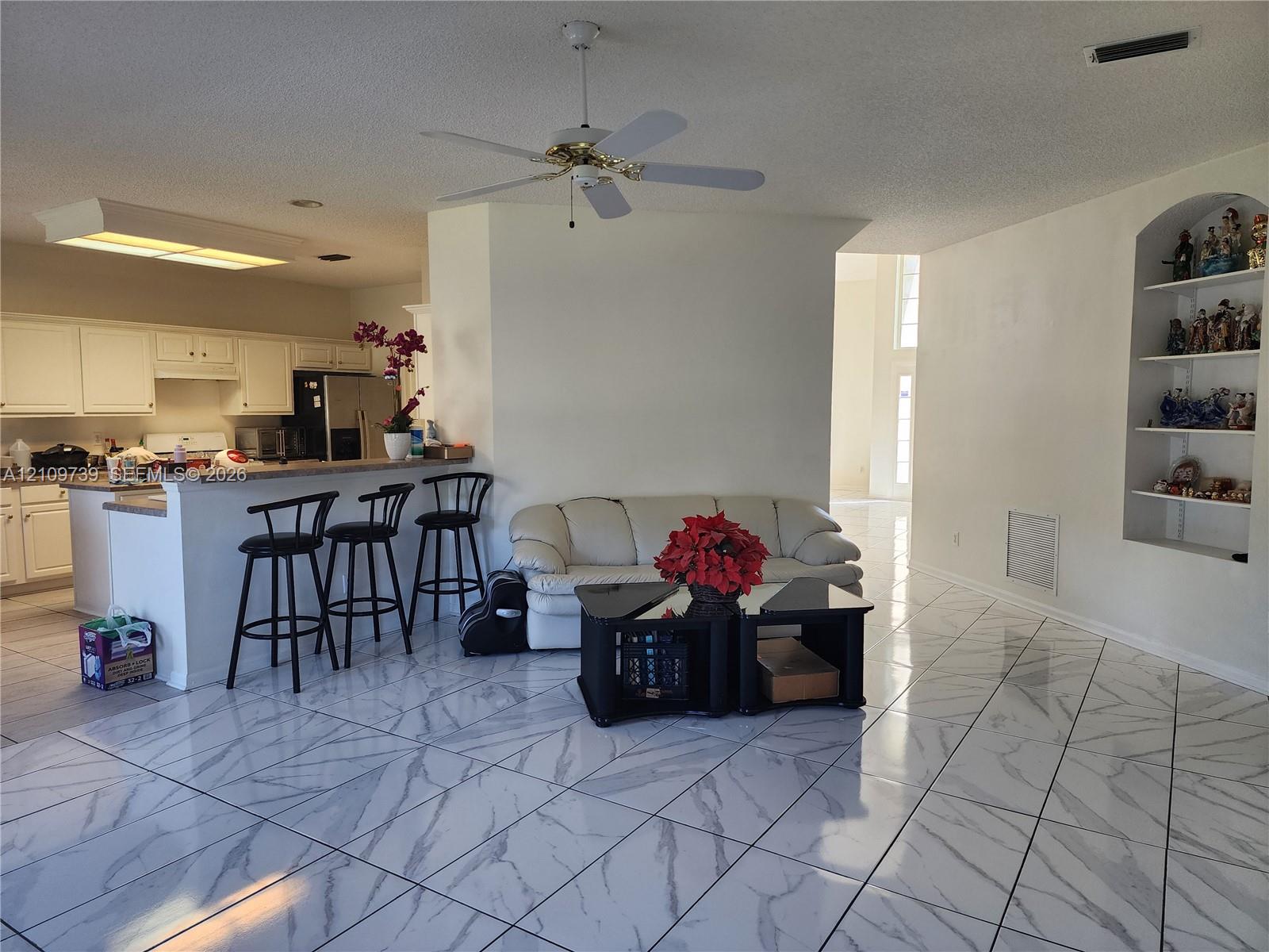 Open-concept interior featuring large-format tile flooring with marble-patterned veining, white cabinetry, a built-in arched display niche, and a ceiling fan with light fixture Open-concept interior featuring large-format tile flooring with marble-patterned veining, white cabinetry, a built-in arched display niche, and a ceiling fan with light fixture