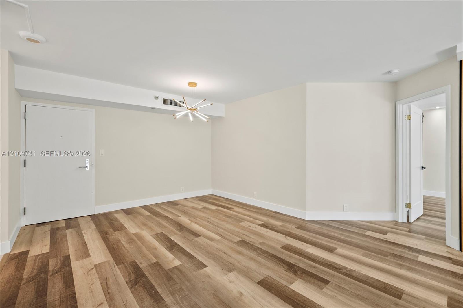 Interior space featuring wood-finish flooring, a modern multi-arm starburst chandelier, and smooth-finish walls Interior space featuring wood-finish flooring, a modern multi-arm starburst chandelier, and smooth-finish walls