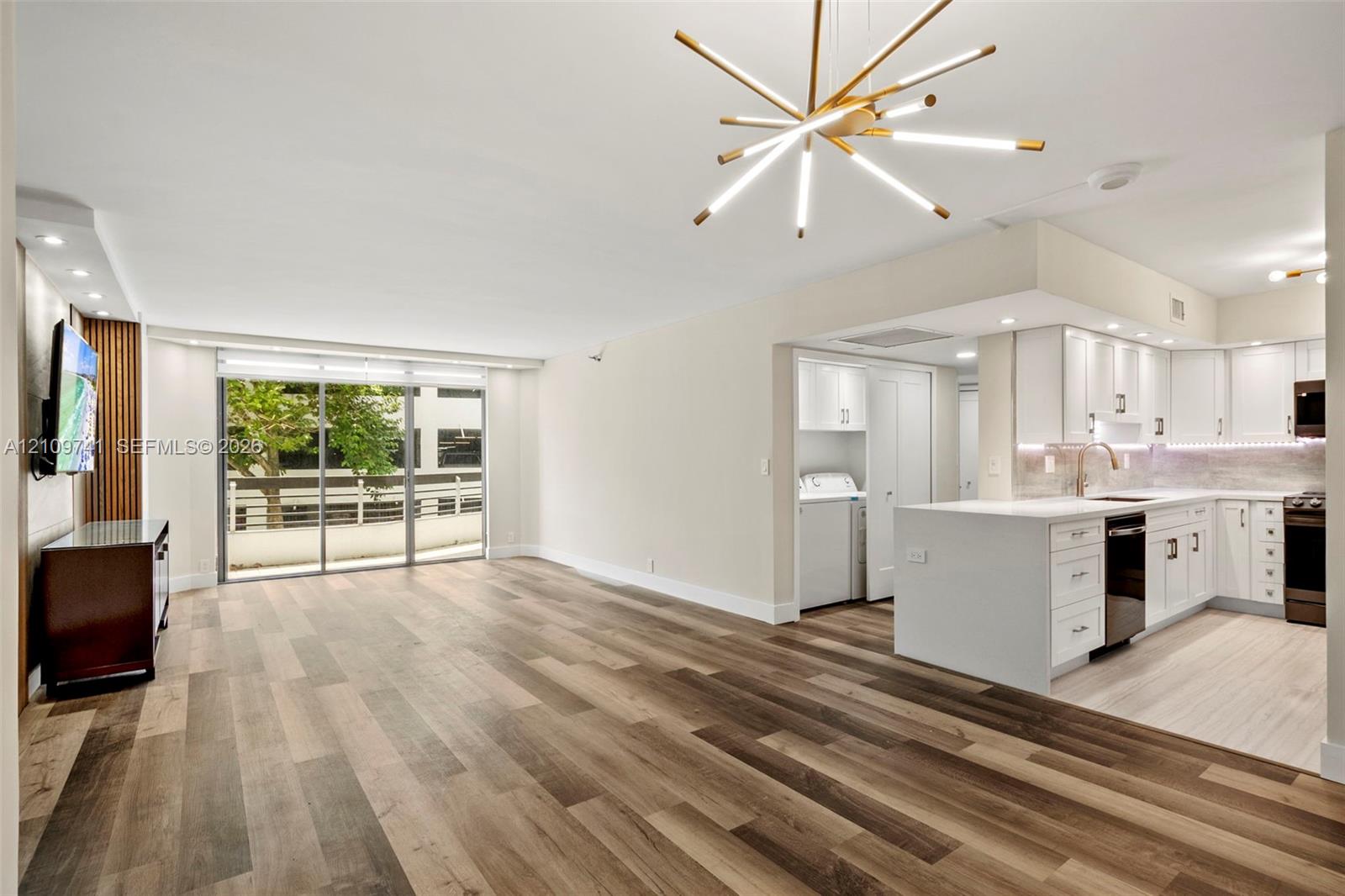 Open-concept area featuring wood-finish flooring, a modern sputnik-style chandelier, and floor-to-ceiling sliding glass doors Open-concept area featuring wood-finish flooring, a modern sputnik-style chandelier, and floor-to-ceiling sliding glass doors