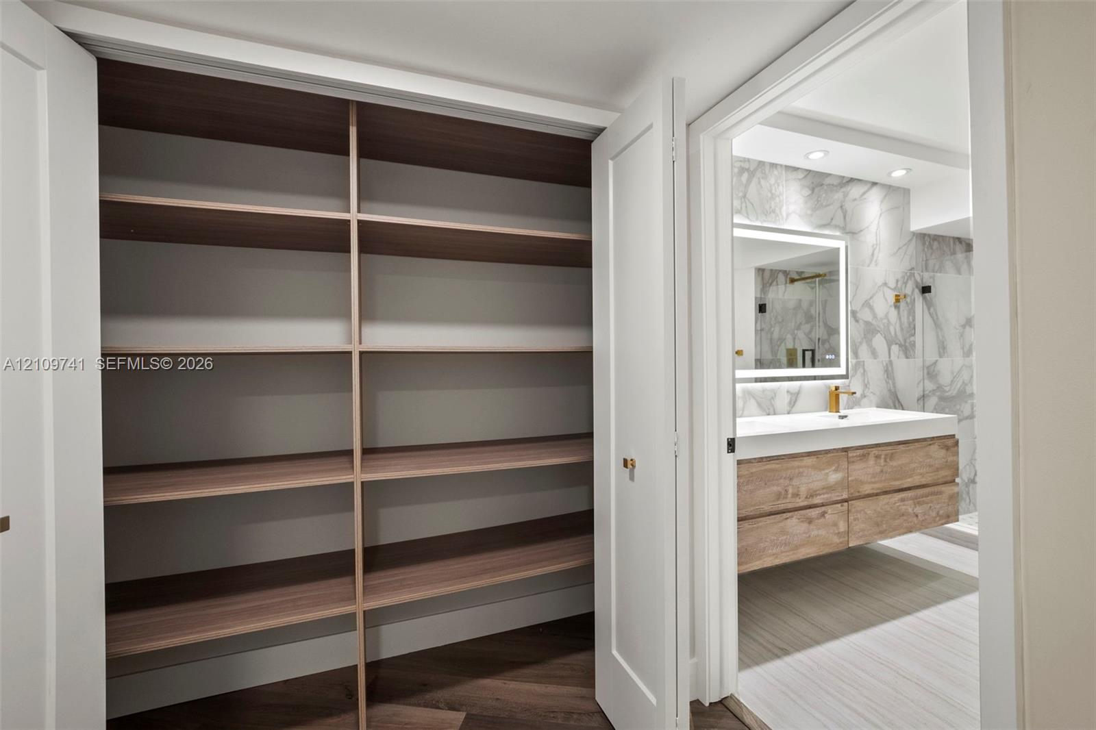 Built-in storage closet featuring wood-finish shelving, and bathroom with a floating wood-finish vanity, integrated rectangular sink, wall-mounted faucet, and stone-finish wall tile