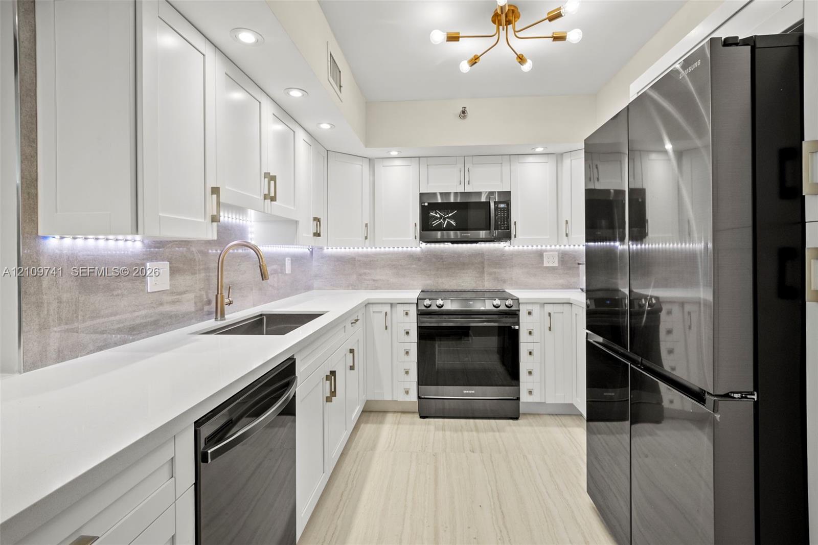 Kitchen featuring white shaker-style cabinetry, stainless steel appliances, stone-surface countertops, under-cabinet lighting, and wood-finish flooring Kitchen featuring white shaker-style cabinetry, stainless steel appliances, stone-surface countertops, under-cabinet lighting, and wood-finish flooring