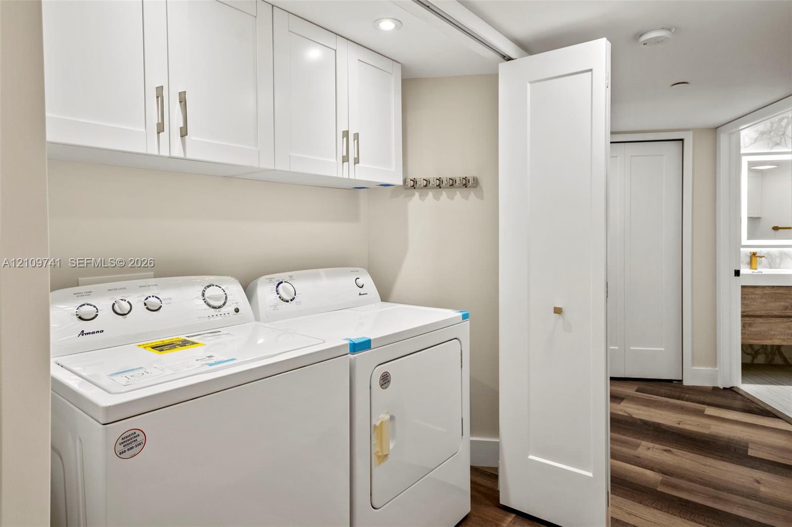 Laundry area featuring white shaker-style wall cabinetry, recessed lighting, and wood-finish flooring