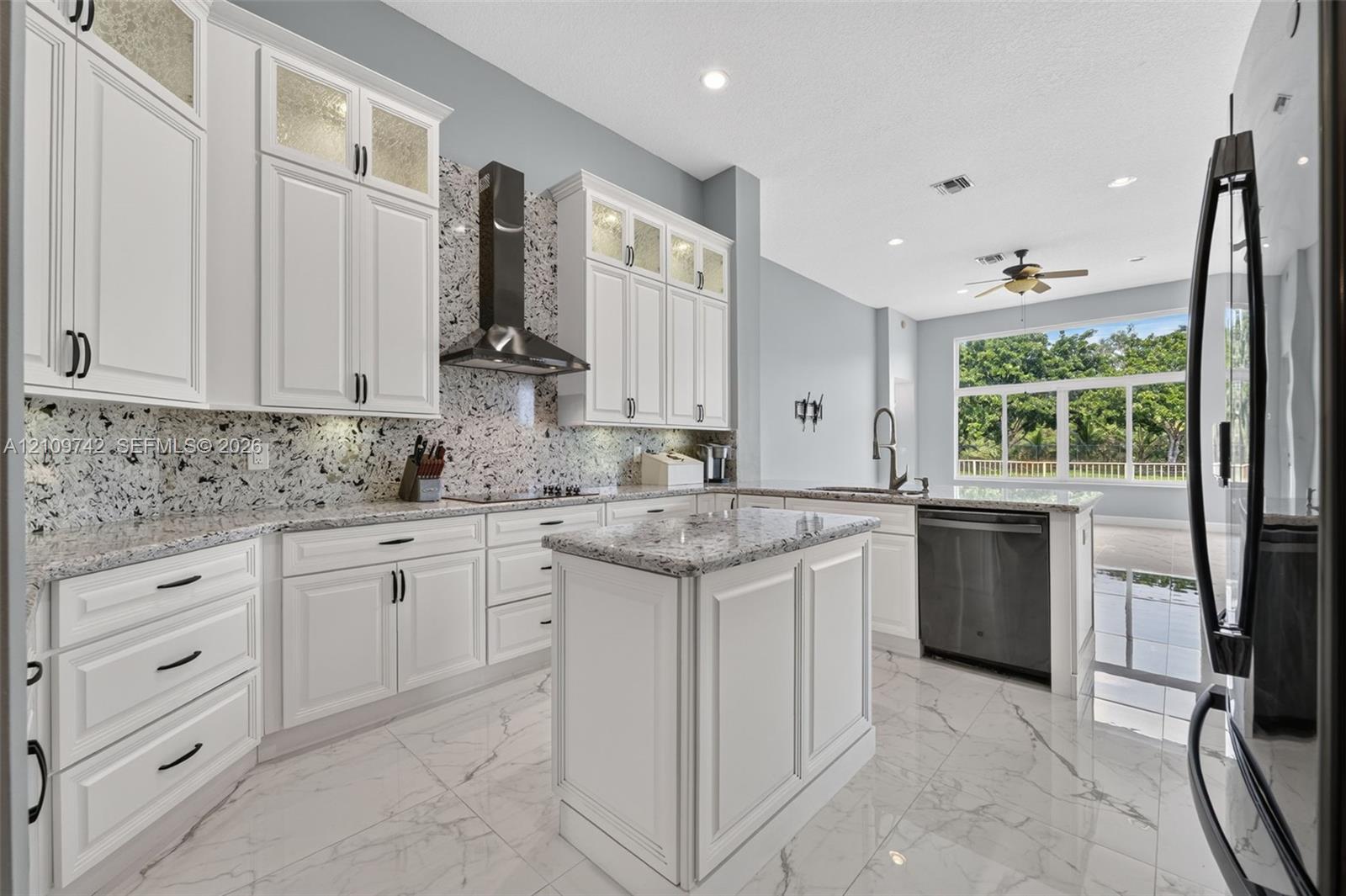 Kitchen featuring white cabinetry with glass-panel upper doors, stone-finish countertops, full-height decorative backsplash, stainless steel range hood, and large-format tile flooring