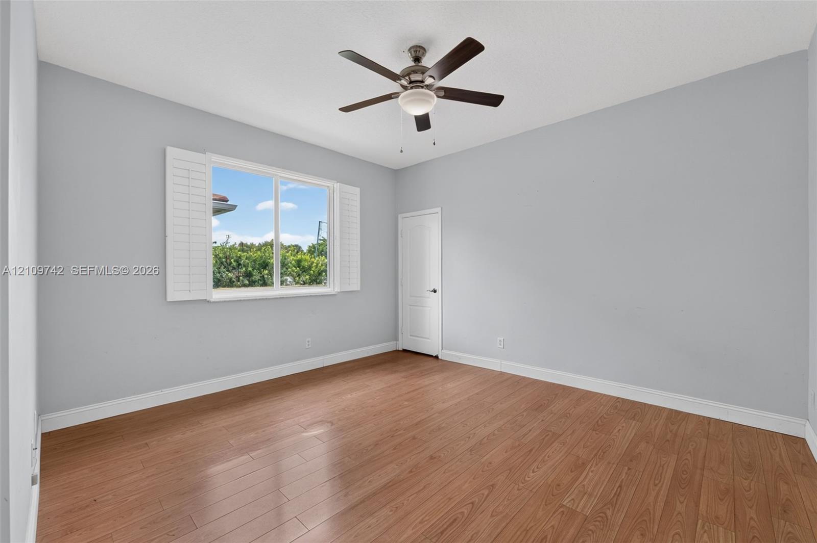 Room featuring wood-finish flooring, plantation shutters, and a central ceiling fan with an integrated light fixture
