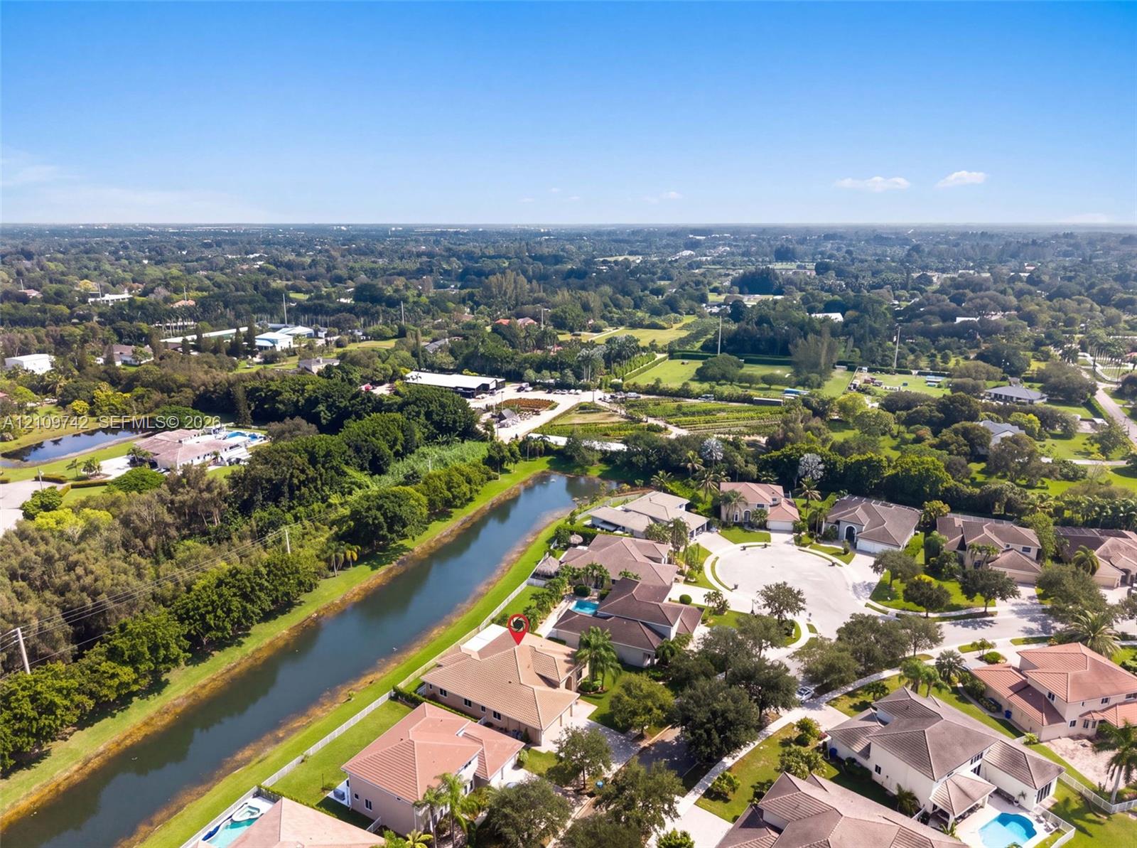 Aerial perspective featuring a waterfront property with a tile roof, paved driveway, and mature landscaping