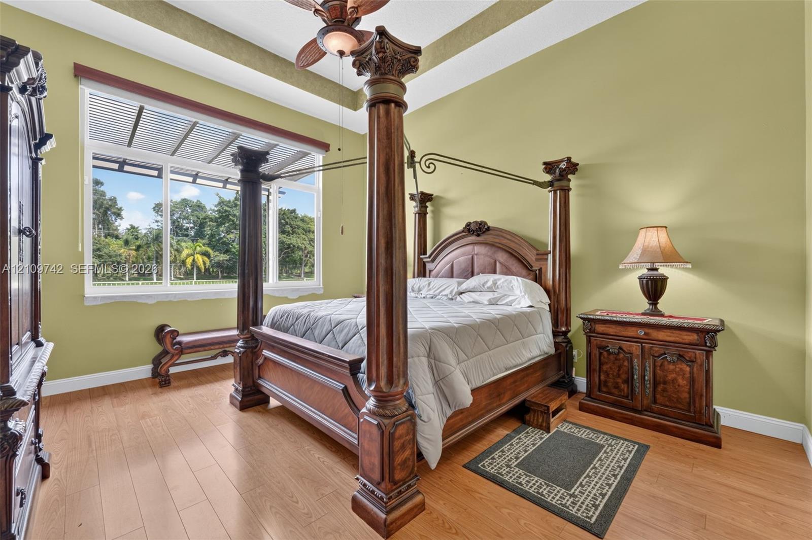 Tray ceiling with crown molding, wood-finish flooring, and large window with exterior landscape backdrop