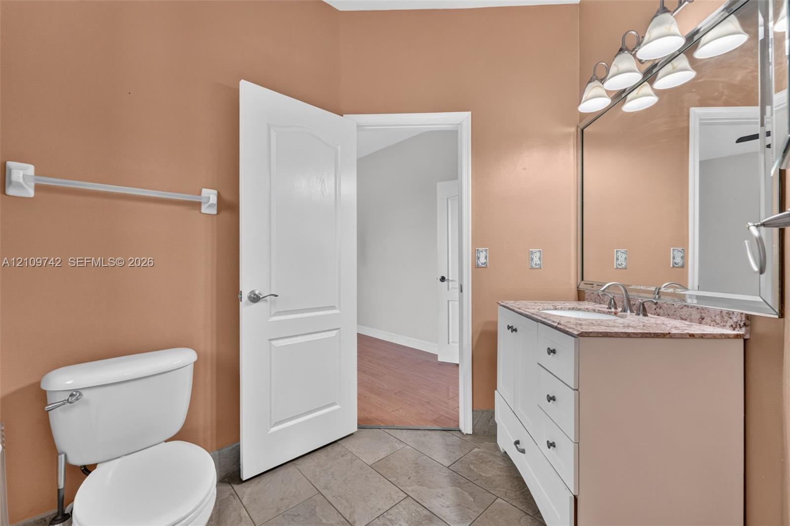 White vanity cabinet with stone-finish countertop, undermount sink, multi-light fixture, and ceramic tile flooring