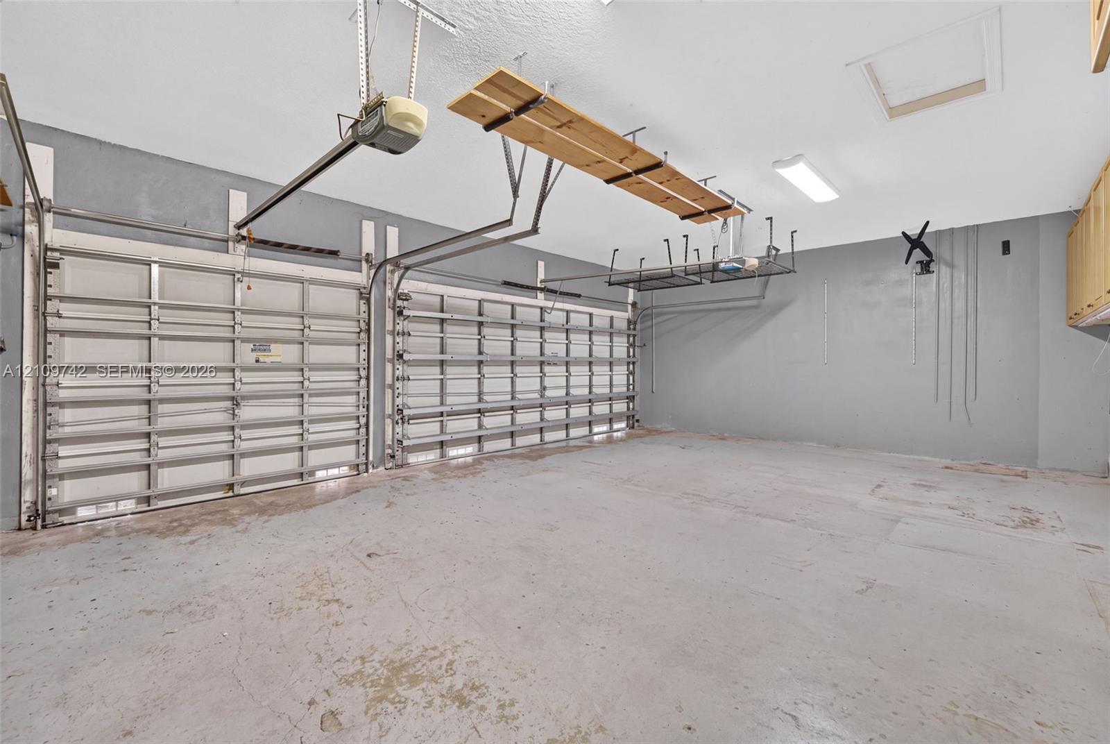 Two-car garage featuring dual overhead metal doors, painted concrete flooring, ceiling-mounted storage racks, and built-in wall cabinetry