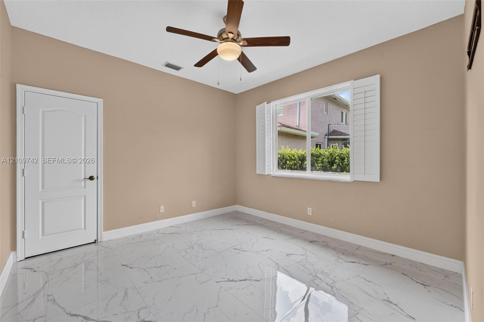 Large-format tile flooring with a veined pattern, multi-panel interior door, and a ceiling-mounted fan with integrated lighting