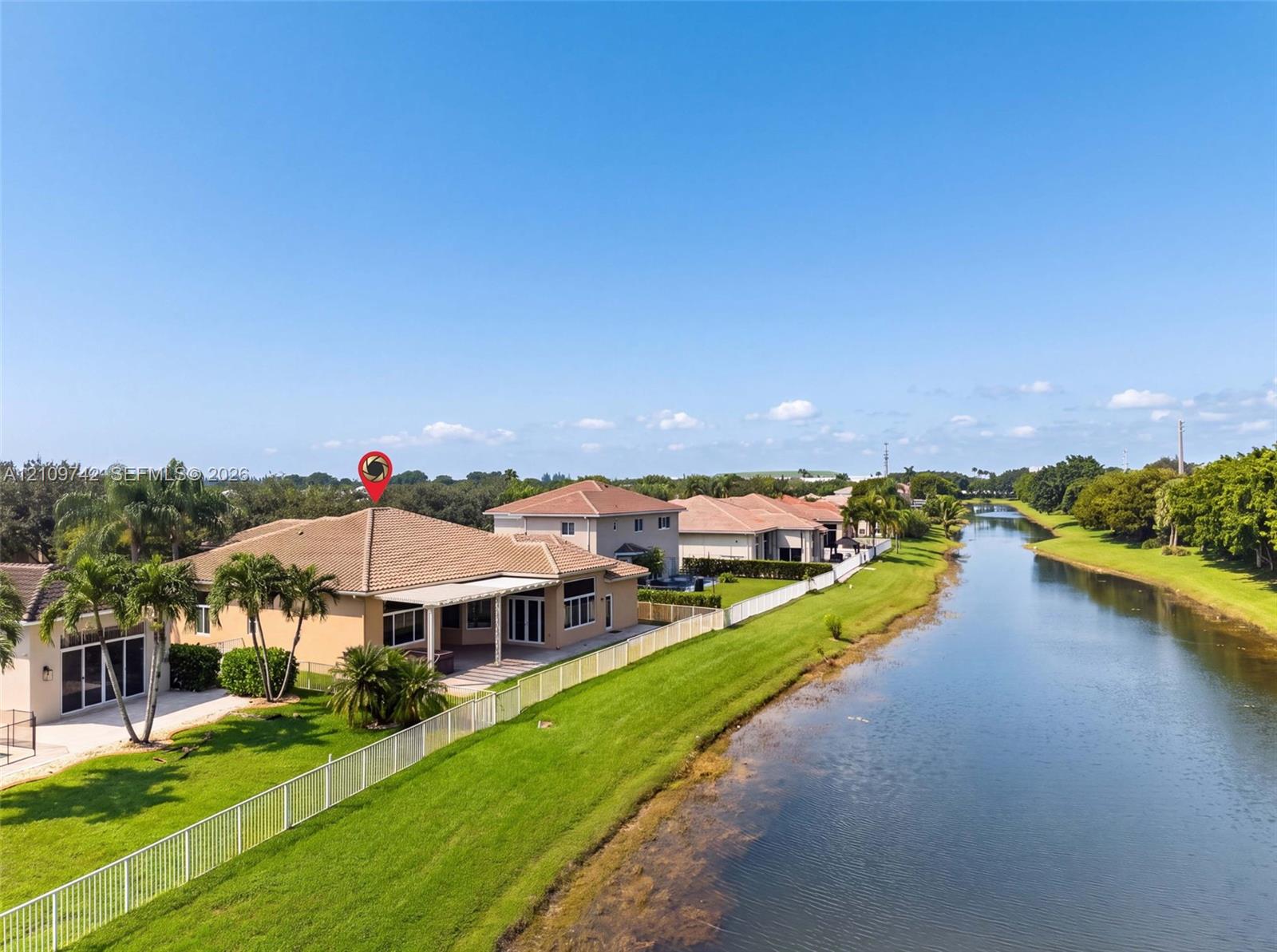 Waterfront property featuring a covered patio, tile roof, and perimeter fencing along a canal