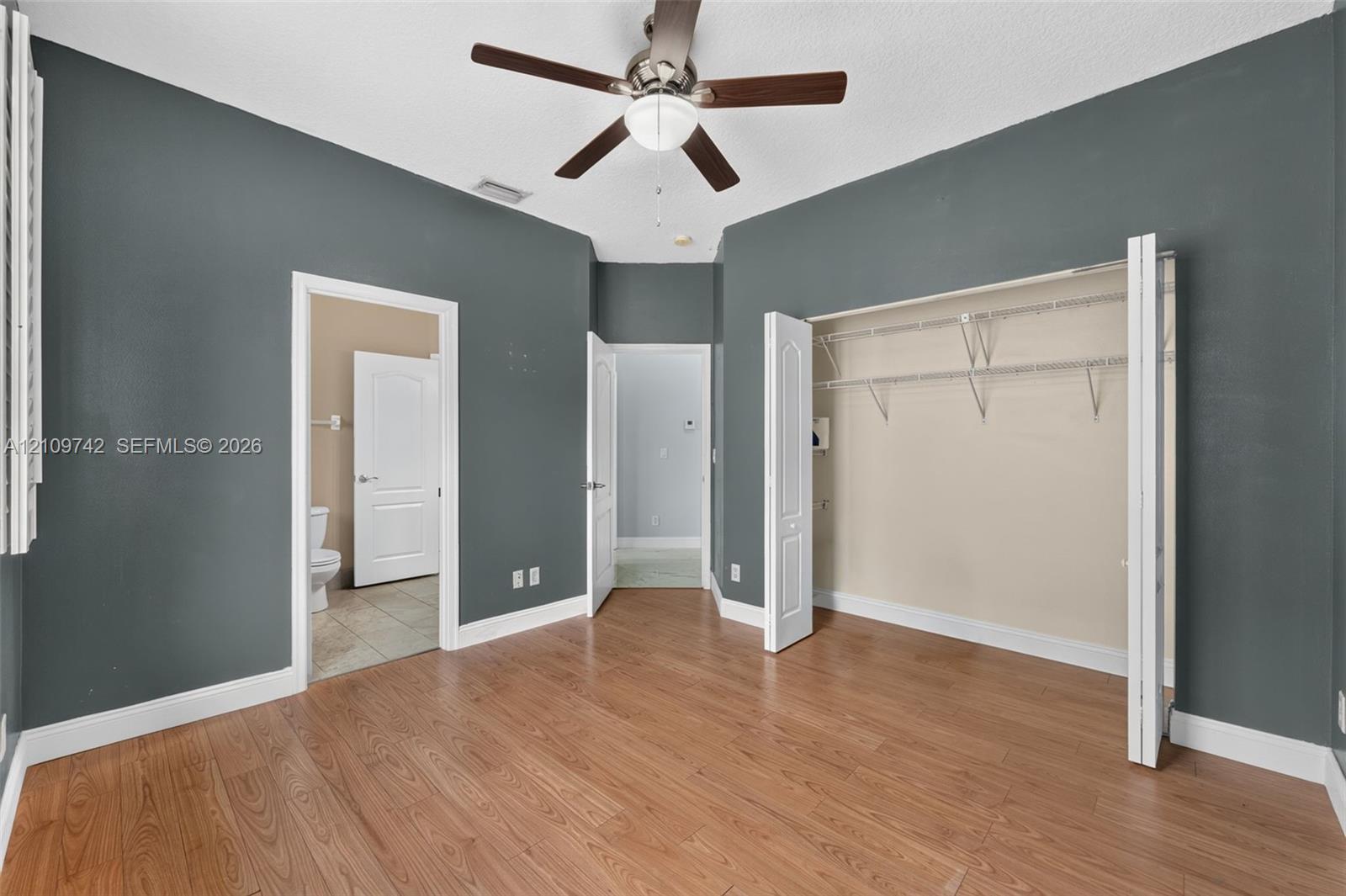 Interior space featuring wood-finish flooring, a ceiling fan with integrated lighting, and a reach-in closet with built-in wire shelving
