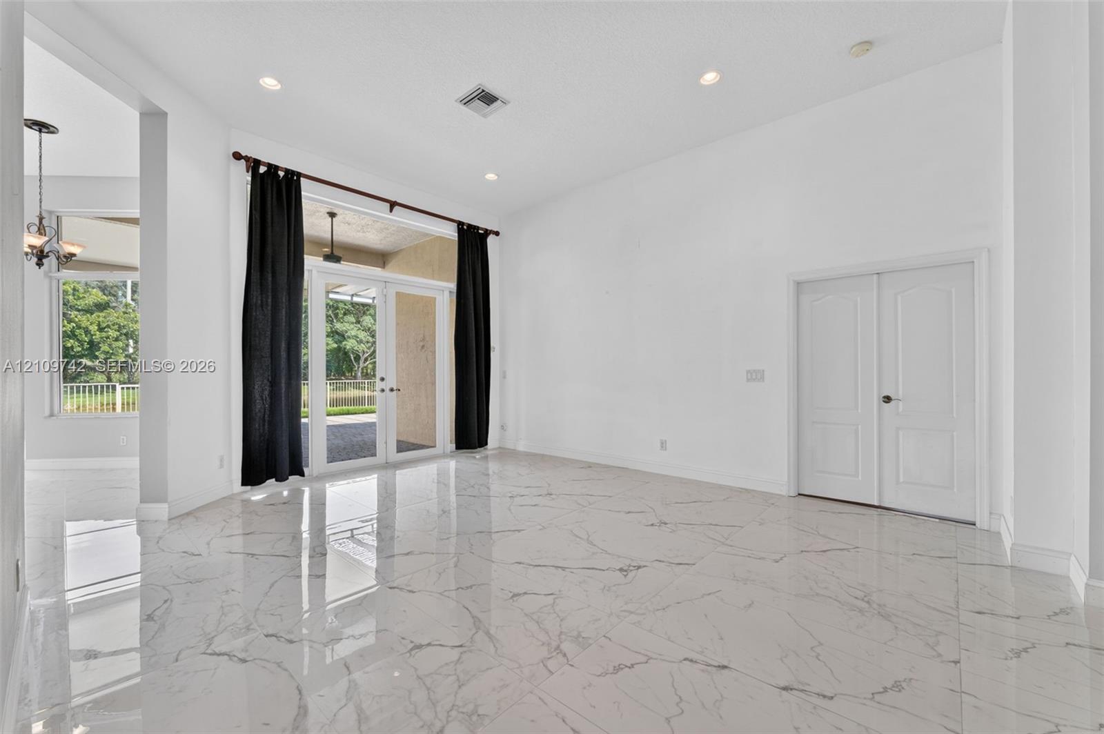 High-ceiling interior featuring polished stone-finish tile flooring, recessed lighting, double French doors, and a double-door entry