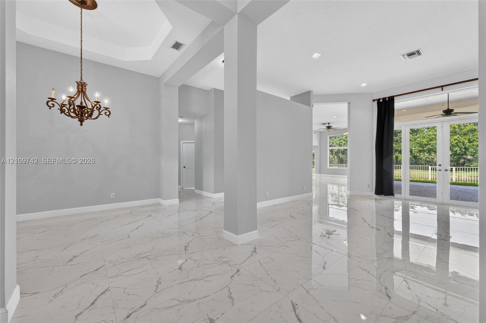 Interior featuring polished stone-finish tile flooring, a tray ceiling, an ornate metal chandelier, architectural support columns, and French doors