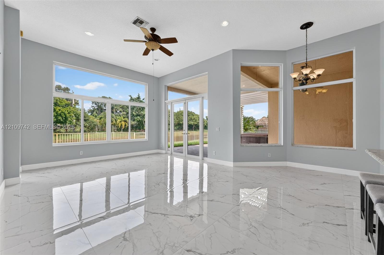 Polished stone-finish flooring, floor-to-ceiling windows, dual glass entry doors, recessed lighting, and a multi-arm chandelier