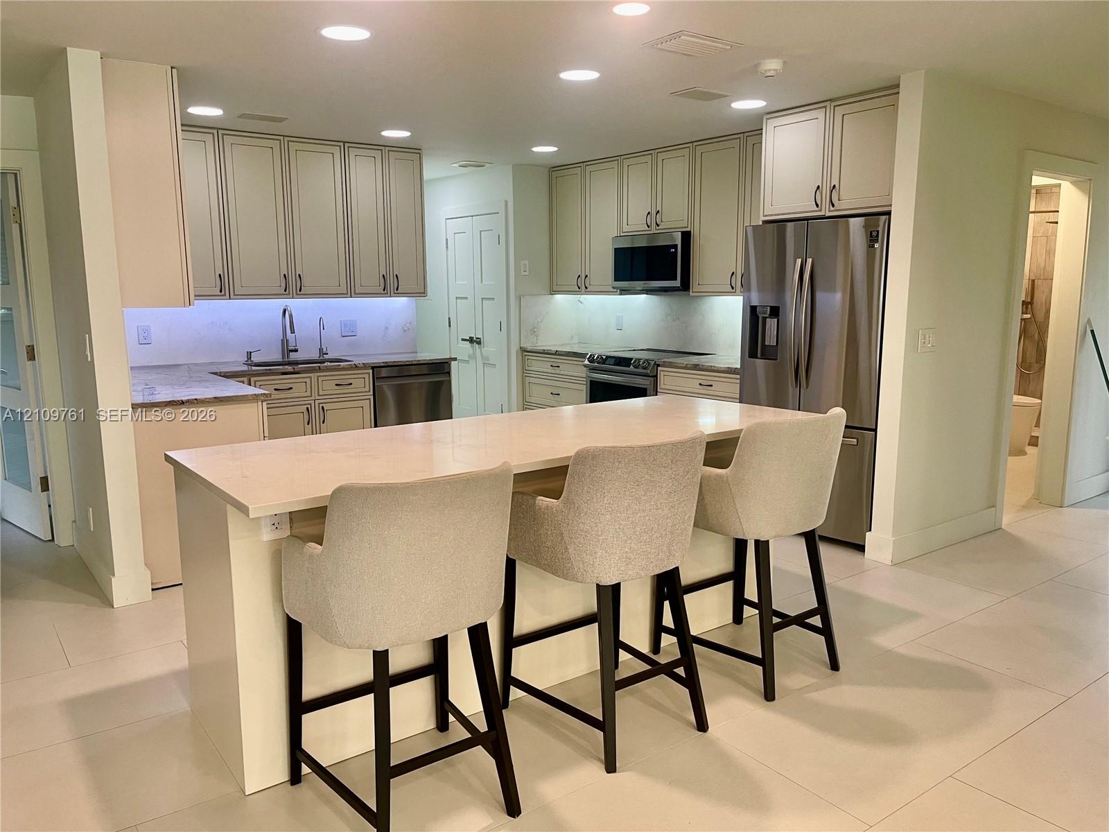 Kitchen featuring an expansive center island with quartz countertops, custom cabinetry, stainless steel appliances, and recessed lighting Kitchen featuring an expansive center island with quartz countertops, custom cabinetry, stainless steel appliances, and recessed lighting