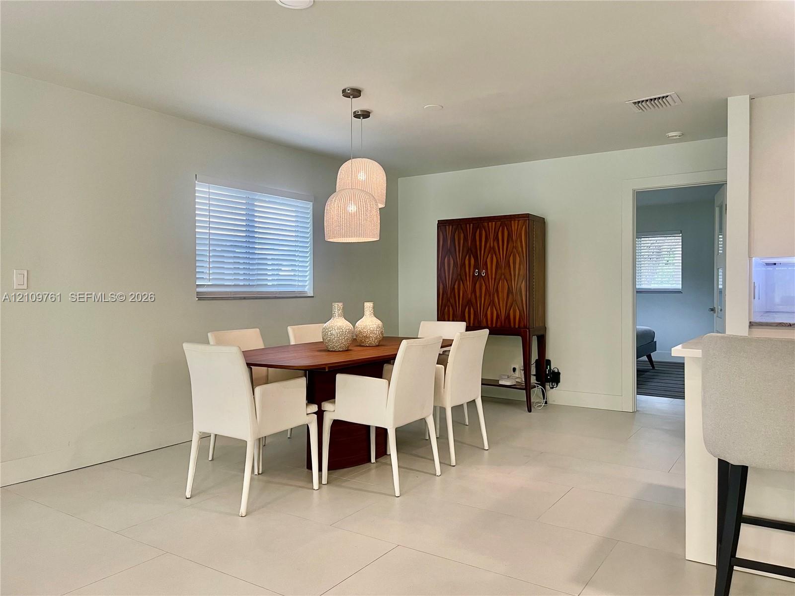 Neutral interior featuring large-format tile flooring, recessed lighting, double pendant lighting fixture, and horizontal blind window treatment Neutral interior featuring large-format tile flooring, recessed lighting, double pendant lighting fixture, and horizontal blind window treatment