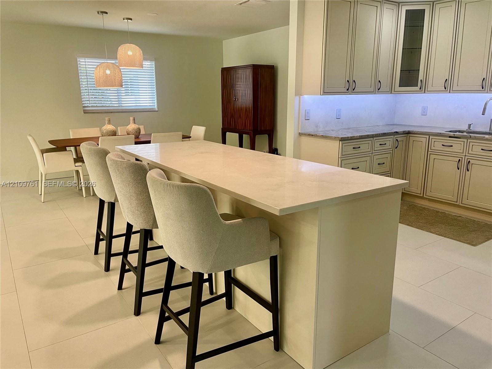 Kitchen featuring an expansive stone-topped island, light-finish cabinetry with glass-front display panels, under-cabinet lighting, and large-format tile flooring