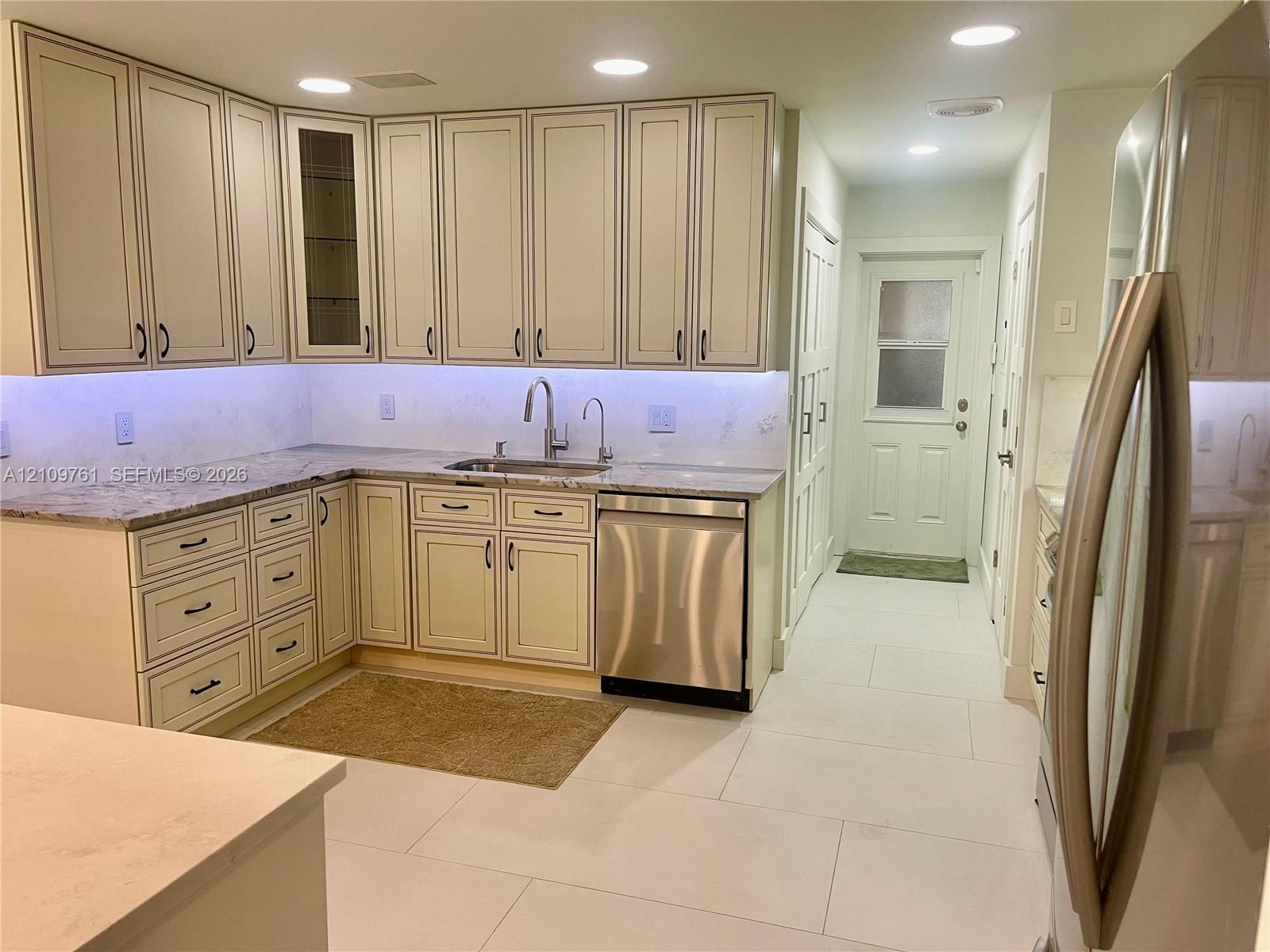 Kitchen featuring shaker-style cabinetry with integrated glass-front doors, stone countertops, stainless steel dishwasher, undermount sink with gooseneck faucet, and porcelain tile flooring Kitchen featuring shaker-style cabinetry with integrated glass-front doors, stone countertops, stainless steel dishwasher, undermount sink with gooseneck faucet, and porcelain tile flooring