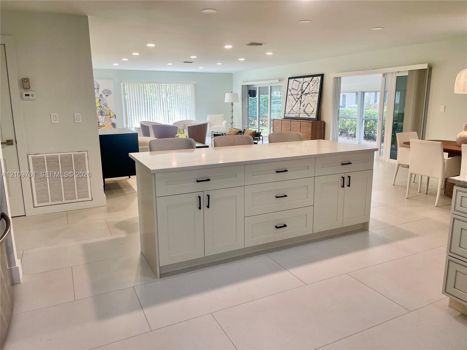 Oversized kitchen island with solid-surface countertops, shaker-style cabinetry, matte black hardware, and large-format tile flooring