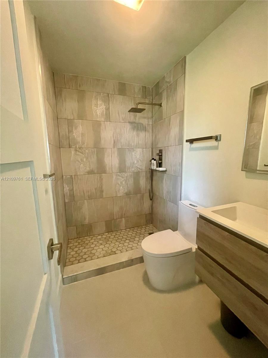 Walk-in shower featuring large-format wall tile, hexagonal floor tile, and a rainfall showerhead, paired with a floating wood-finish vanity and integrated rectangular sink