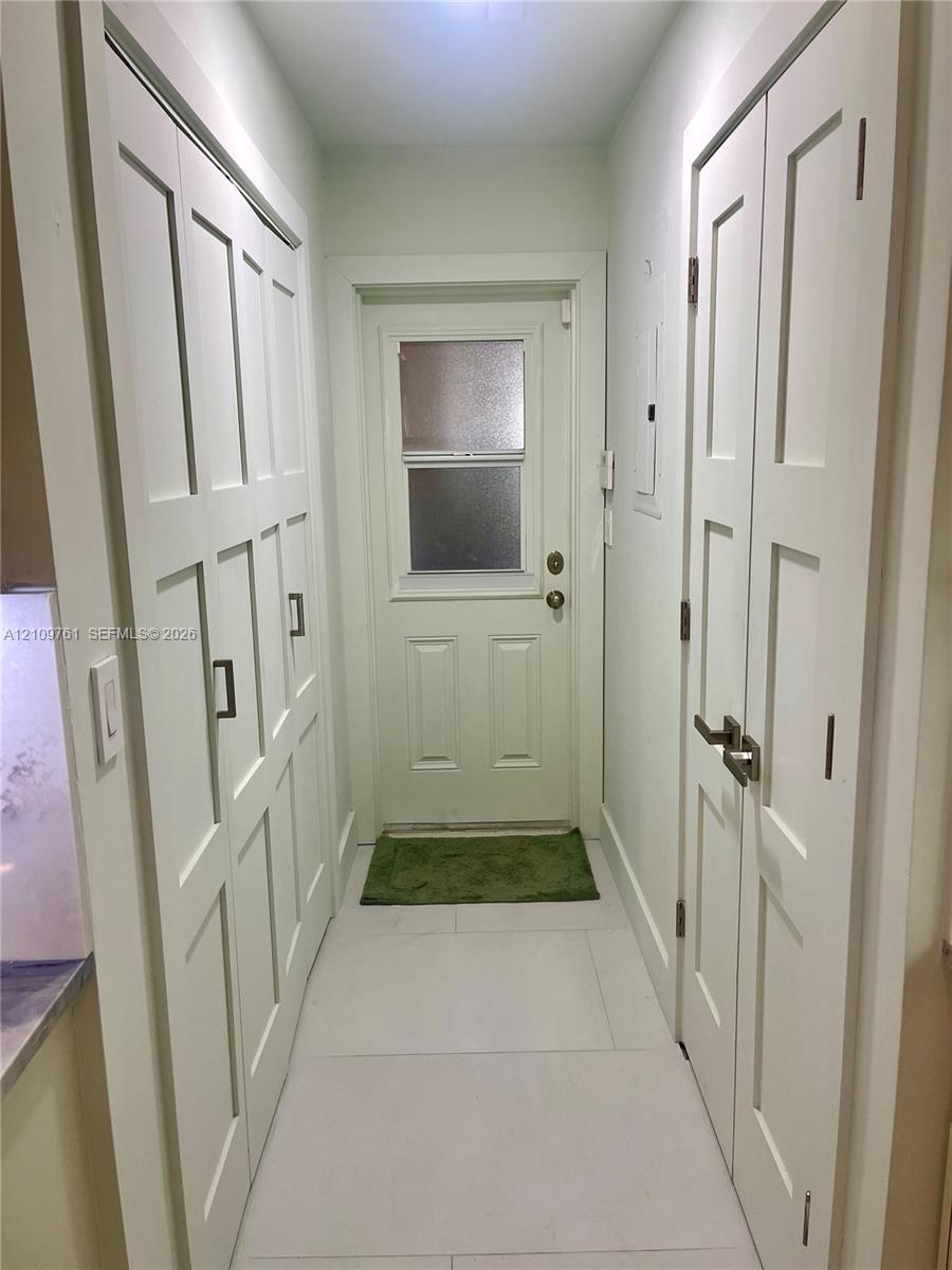 Neutral-toned tile flooring, white Shaker-style built-in cabinetry, and a solid-core door with an inset privacy-glass window