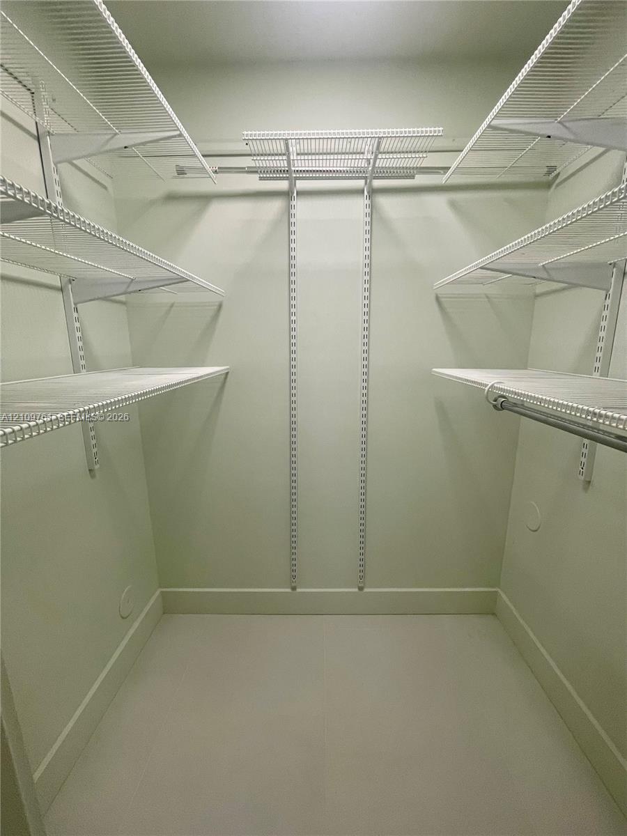 Walk-in closet featuring tiered white wire shelving, adjustable wall-mounted support tracks, and integrated hanging rods