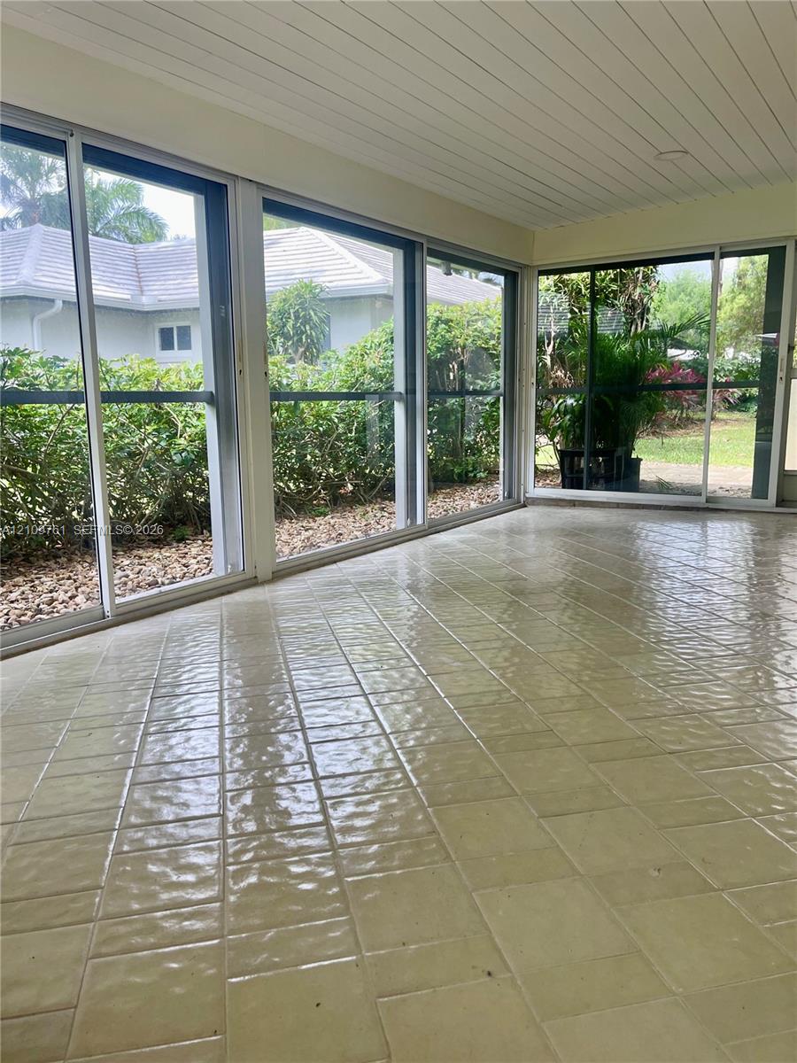 Enclosed sunroom featuring light-colored ceramic tile flooring, beadboard ceiling, and multiple floor-to-ceiling sliding glass doors