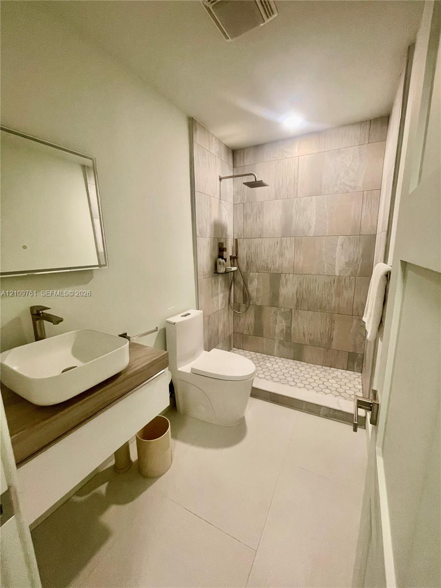 Floating vanity with a rectangular vessel sink and wood-finish countertop, walk-in shower featuring large-format wall tile, hexagonal floor tile, and a rainfall showerhead