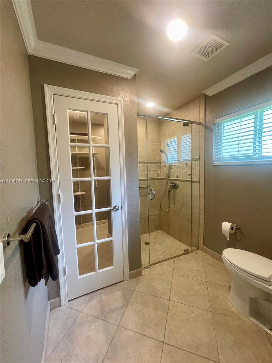 Glass-enclosed walk-in shower with decorative tile inlay, ceramic tile flooring, and French door entry to a closet featuring built-in shelving